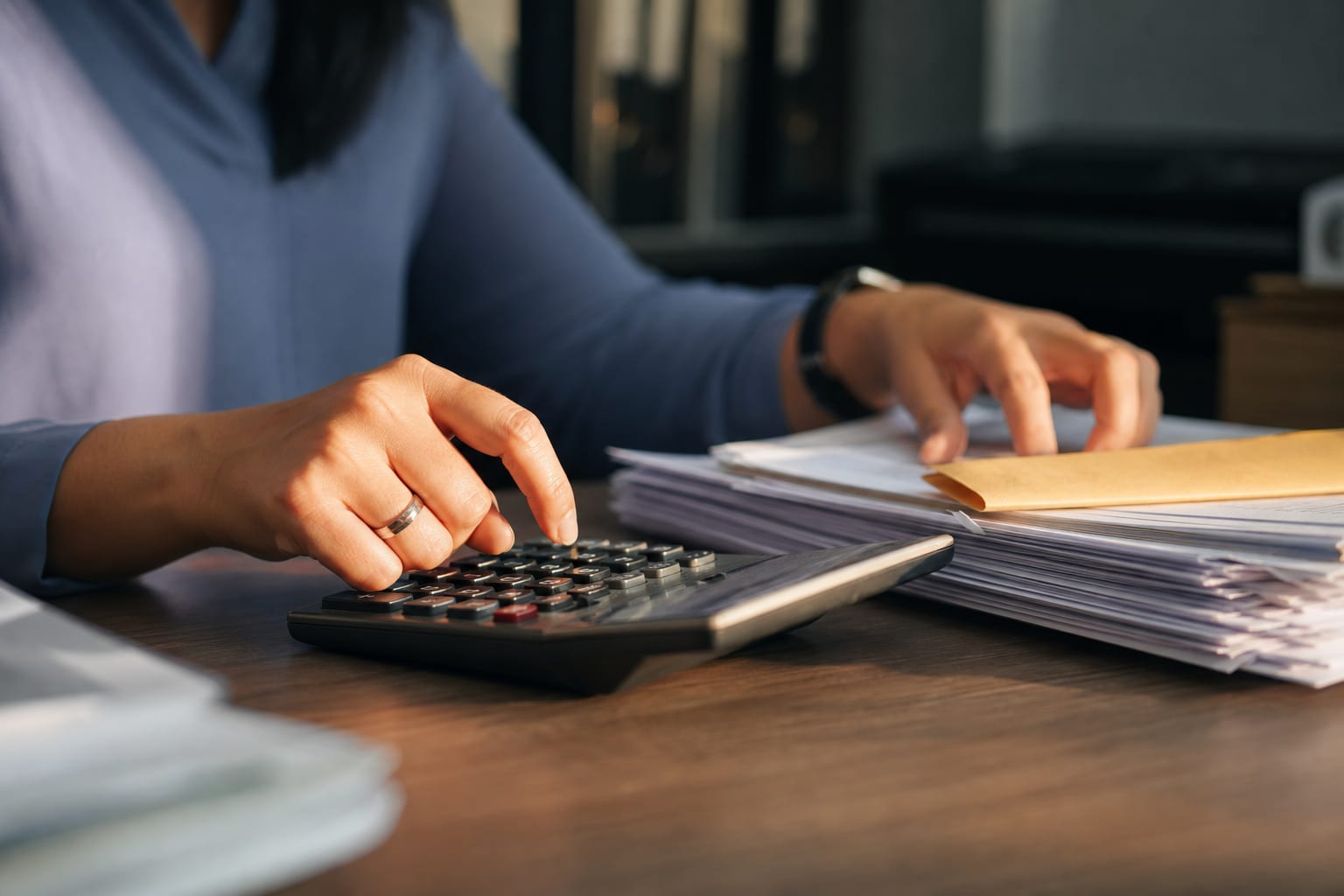 Mãos usando calculadora de mesa ao lado de folhas impressas e envelope em escritório contábil